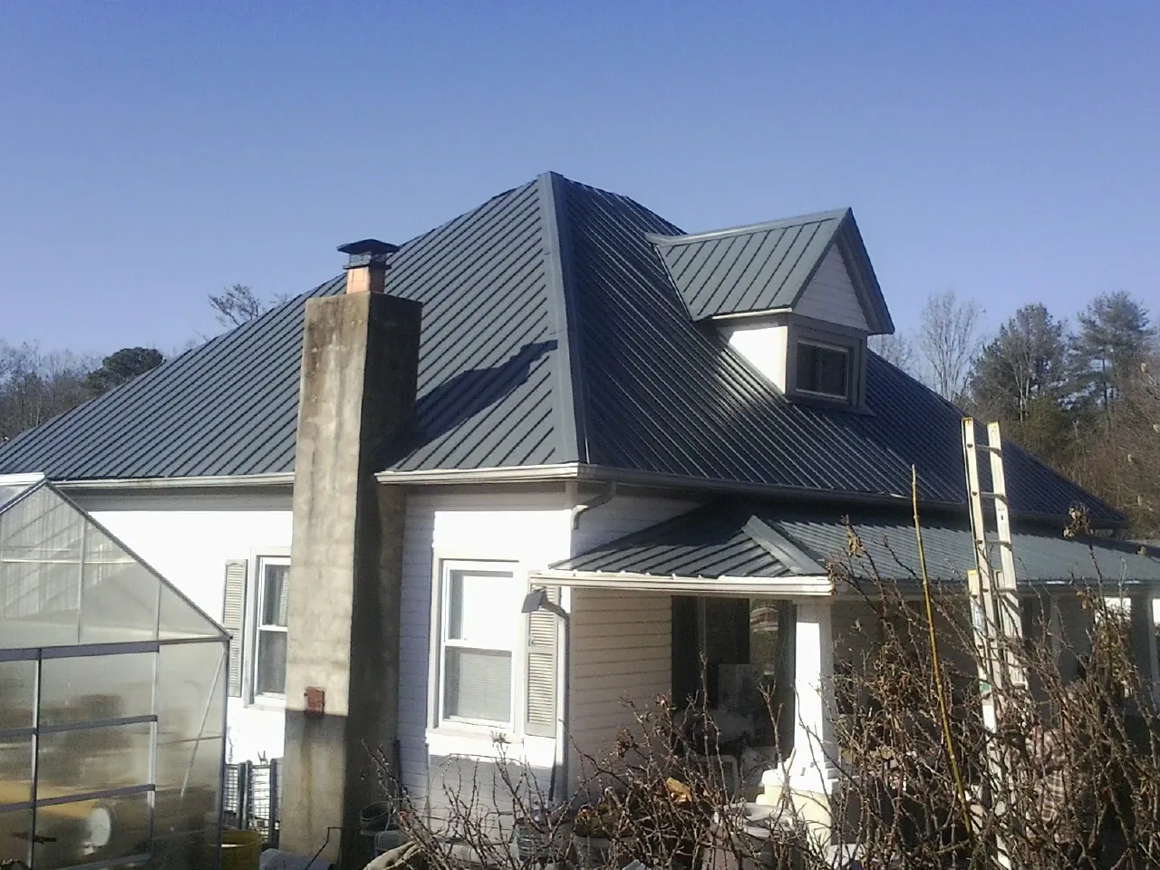 Dark blue standing seam metal roof on a white farmhouse with dormer — Slate & Tile Roof Repair by Roofing Brothers in New Salem