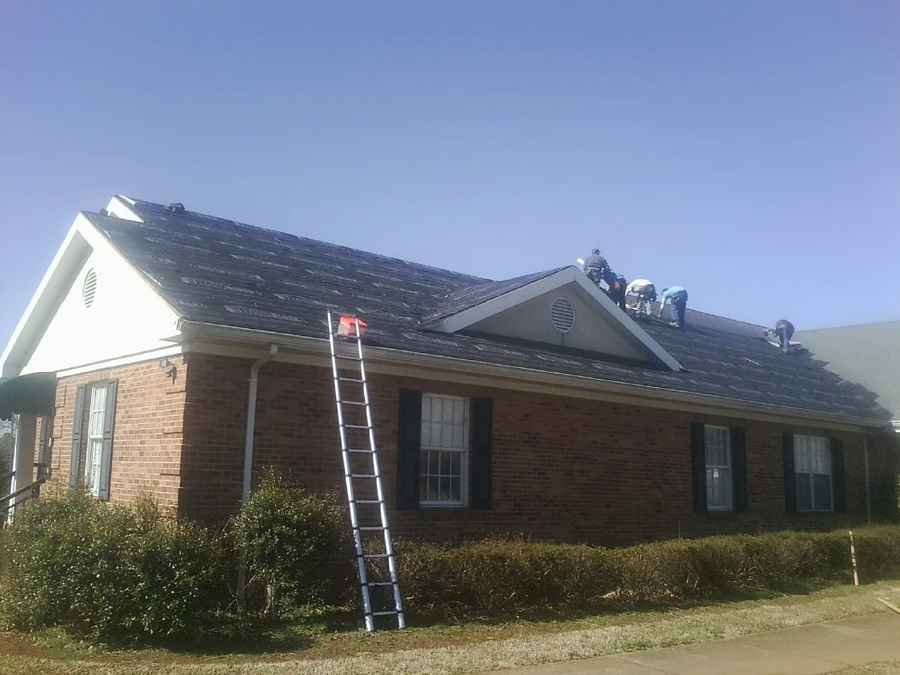 Crew tearing shingles off a brick ranch roof with a ladder set — Metal Roof Repair work by our crew in New Salem