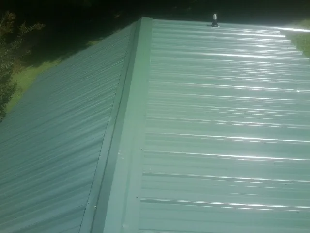 New green metal panels meeting at the ridge of a roof — Flat Roof Repair work by our crew in New Salem