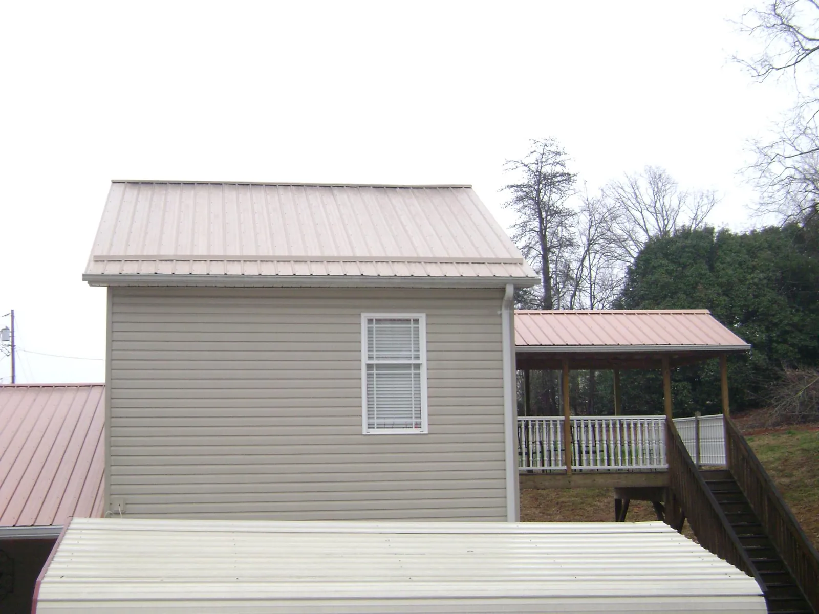 Tan metal roofs on a two story addition and attached porch, from a Roof Replacement job in New Salem